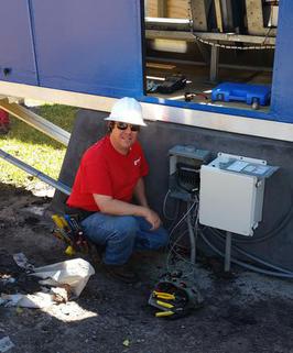 Electrician with hardhat working on electrical box outside.